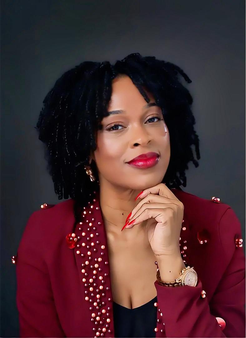 Portrait of Diana Amabelle Nwakanma in a burgundy jacket, smiling slightly with her hand resting beneath her chin