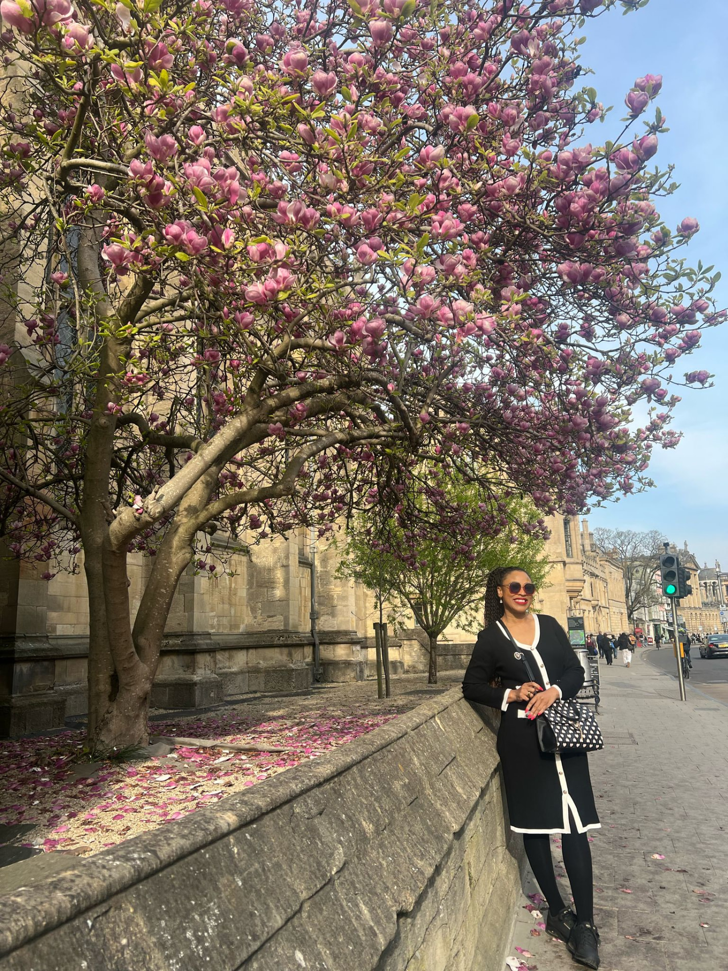 Amabelle standing beneath a large flowering magnolia tree on an Oxford street, historic stone architecture behind her