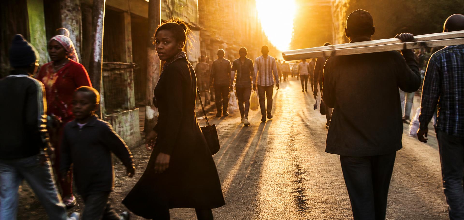 People moving through a city street at golden hour, a woman glancing back mid-stride